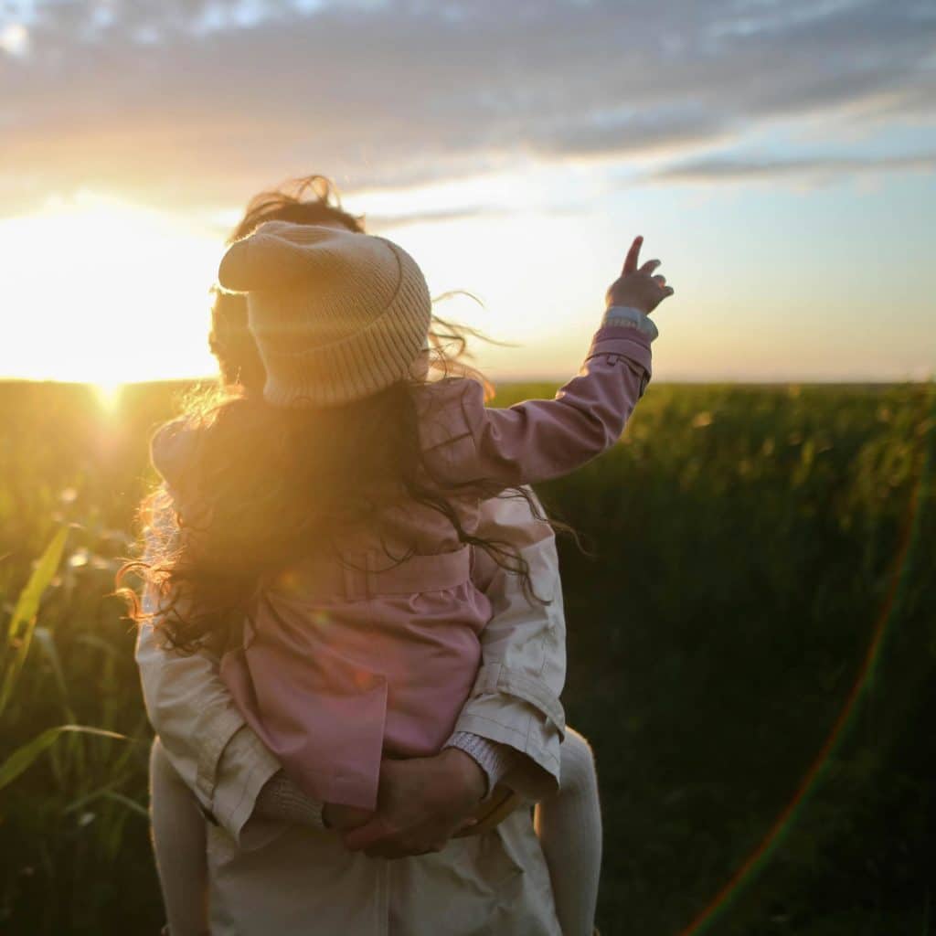 Une maman avec son enfant dans les bras dans un champ au coucher du soleil