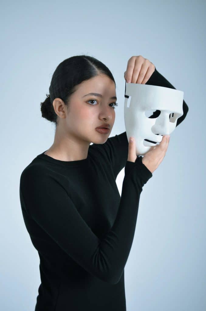 Une femme tient un masque blanc devant son visage